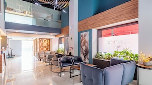A modern lobby with seating areas, a reception desk, and a staircase leading to an upper level.