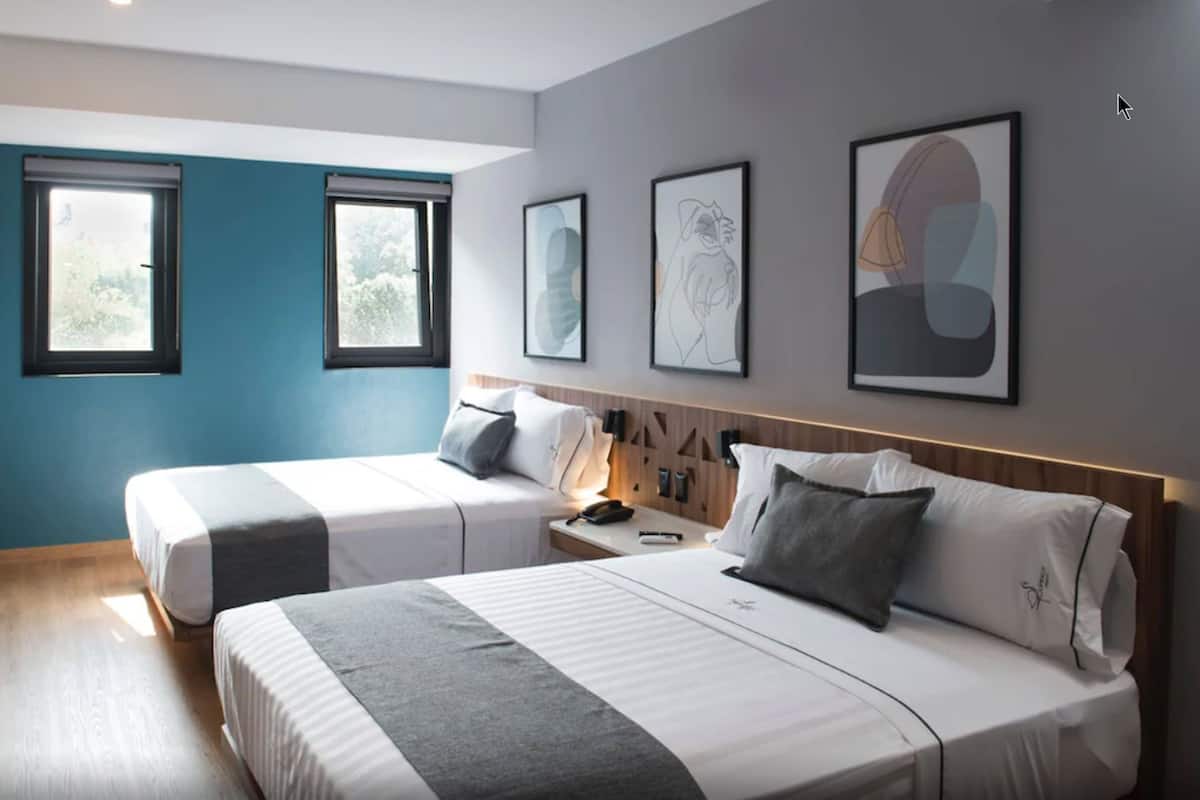 Habitación de hotel con dos camas, piso de madera y obras de arte en las paredes.