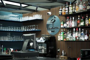Zona de bar con estantes llenos de botellas de licores, vasos y una máquina de café.