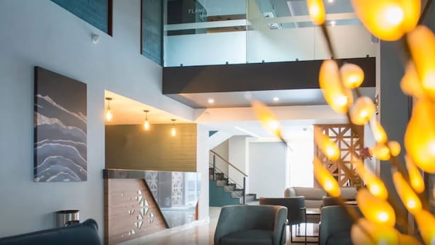A modern interior with a staircase leading to an upper level, a seating area with sofas, and a decorative wall piece.