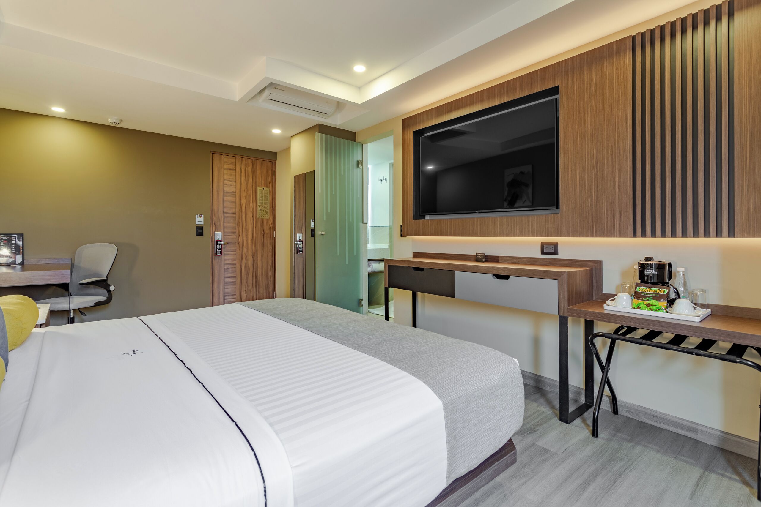 A hotel room with a bed, desk, chair, TV, and a coffee station.