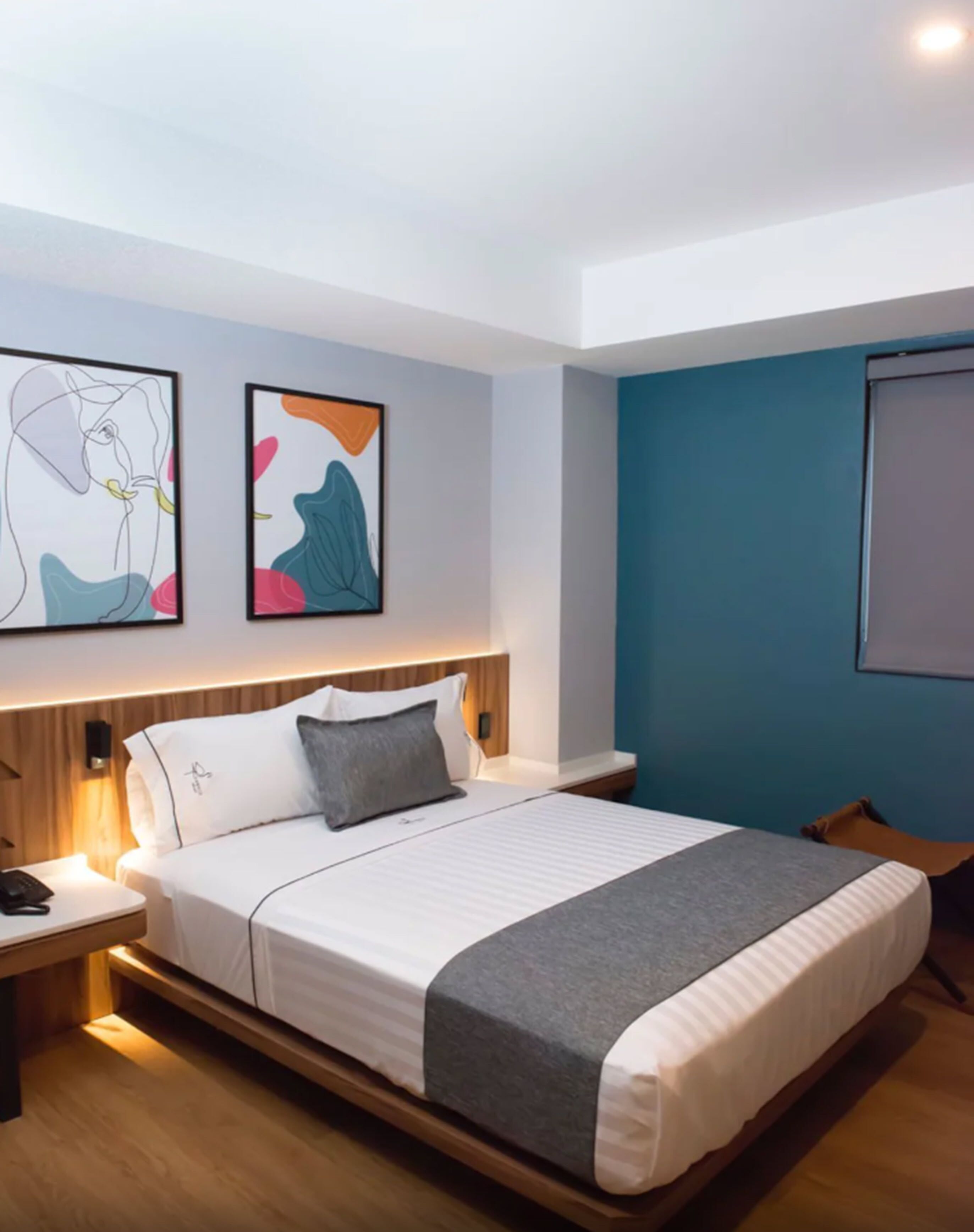 Une chambre d’hôtel moderne avec un grand lit, une table de chevet, une commode et deux tableaux abstraits accrochés au mur.