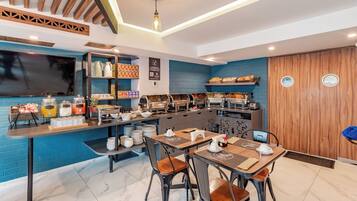 A modern cafe with a blue brick wall, wooden ceiling beams, and a buffet counter with various food items.