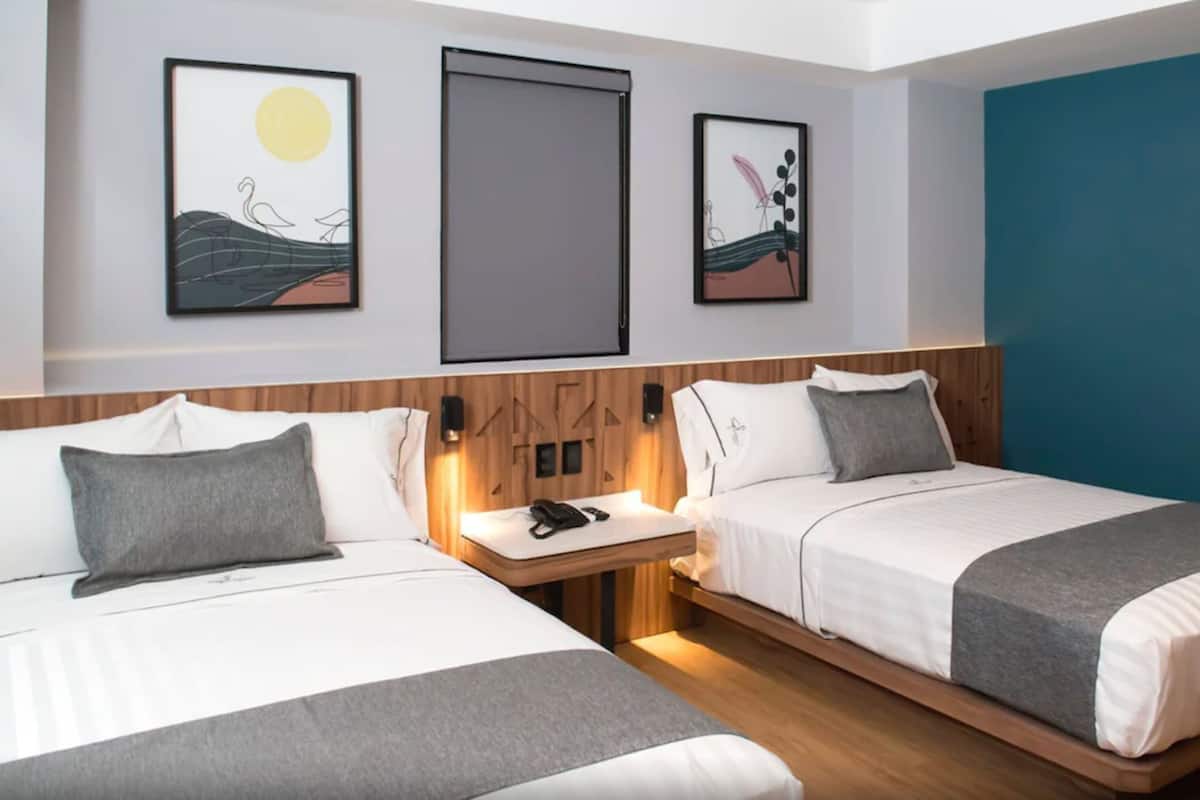 Habitación de hotel con dos camas, cabecero de madera, mesita de noche y decoración en la pared.