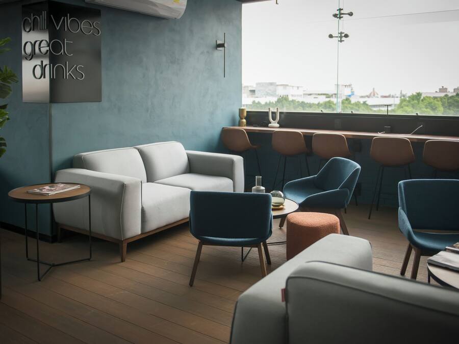 Un espacio lounge moderno con un sofá, sillas y una barra con taburetes. Un letrero dice 'ambiente relajado, excelentes bebidas'.