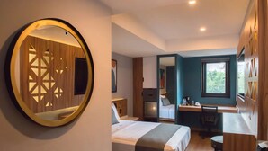 A modern hotel room with a large mirror, a bed, a desk, and a view of greenery outside.
