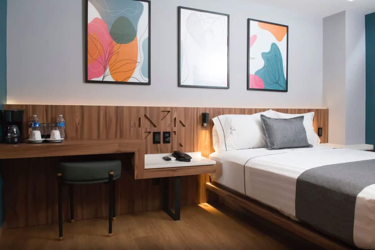 Habitación de hotel con cama, escritorio con silla y dos cuadros abstractos en la pared.
