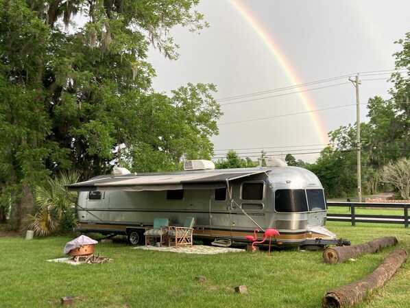 A recreational vehicle (RV) parked in a grassy area with a rainbow in the background.