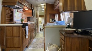 Eine kleine Küchenzeile in einem Wohnmobil mit Holzschränken, einem Herd und einem Fernseher.