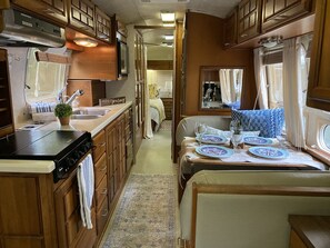 A compact RV kitchen with wooden cabinets, a stove, and a sink.