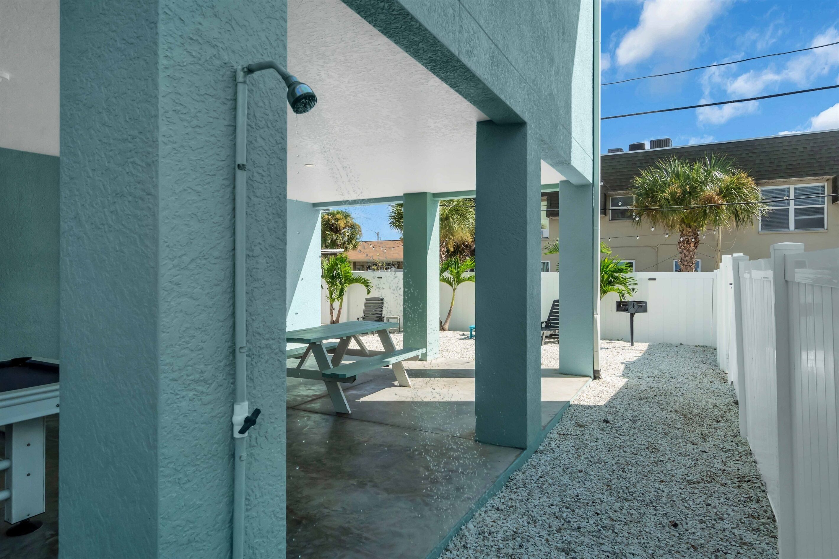 Un espace extérieur abrité, doté d’un sol en béton, d’une table de pique-nique et d’une clôture blanche.