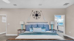 A bedroom with a large bed, a wall-mounted compass, and a view of the ocean through an open door. - Luxury Beachhouse W/ Direct Ocean Views Sleeps 12 (Madeira Beach)
