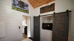A hallway with white paneled walls, a wooden ceiling, and a sliding barn-style door with a mounted television. - Sweet Creek Retreat-Luxury Tiny Cabin-View-WIFi-Hot tub-Firepit Area-Smart TVs (Turtletown)