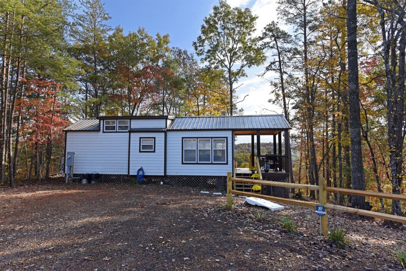 A small cabin with a porch, surrounded by trees with autumn foliage.