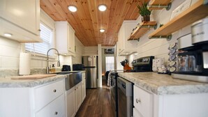 A modern kitchen with white cabinetry, wooden ceiling, and built-in appliances. - Sweet Creek Retreat-Luxury Tiny Cabin-View-WIFi-Hot tub-Firepit Area-Smart TVs (Turtletown)