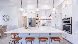 A modern kitchen with a large island, stainless steel appliances, and pendant lighting.