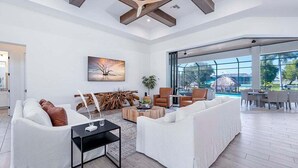 A spacious living room with a large window, white sofas, a coffee table, and a wooden ceiling structure.
