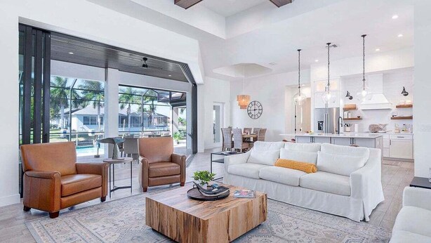 A spacious living area with a white sofa, two leather armchairs, and a wooden coffee table. A large window offers a view of the outdoors.