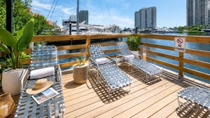 Terraza de madera con sillones de descanso, un letrero que dice 'NO FISHING' y vista al puerto deportivo.