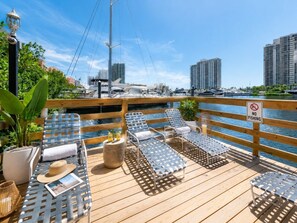A wooden deck with lounge chairs, a 'NO FISHING' sign, and a marina with boats in the background.
