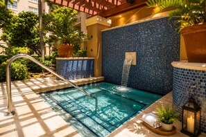 A pool with a waterfall feature, surrounded by potted plants and a tiled wall.