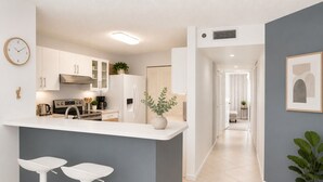 Una cocina moderna con armarios blancos, una isla central con taburetes y un pasillo que conduce a otra habitación.