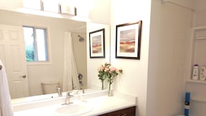 Un baño con un lavamanos blanco, armarios de madera, un espejo grande y dos cuadros en la pared.