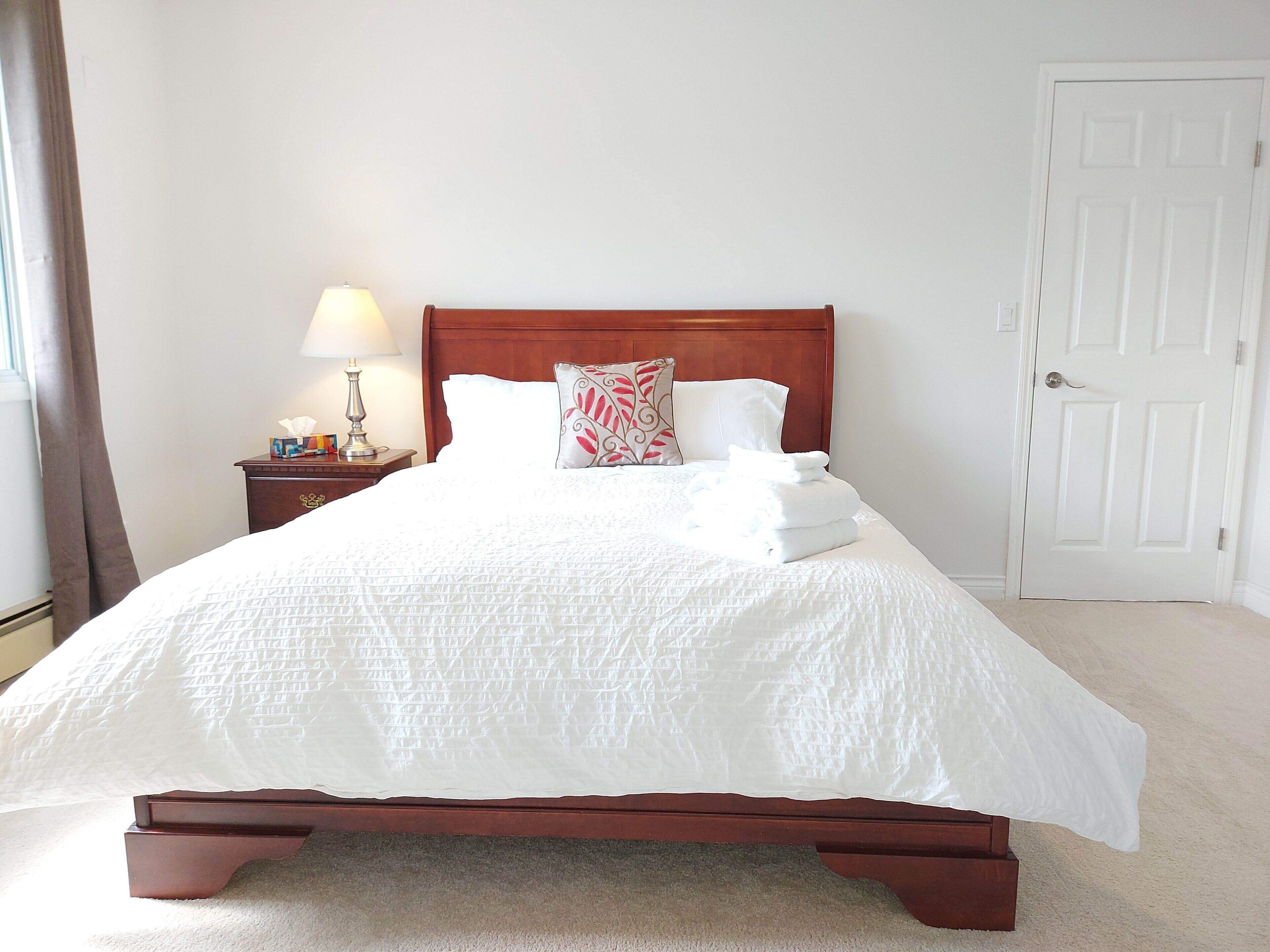 A neatly made bed with white bedding and a wooden headboard, a bedside table with a lamp, and a closed door in a hotel room.