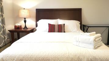A neatly made bed with white bedding, a striped pillow, and a stack of white towels on the side.