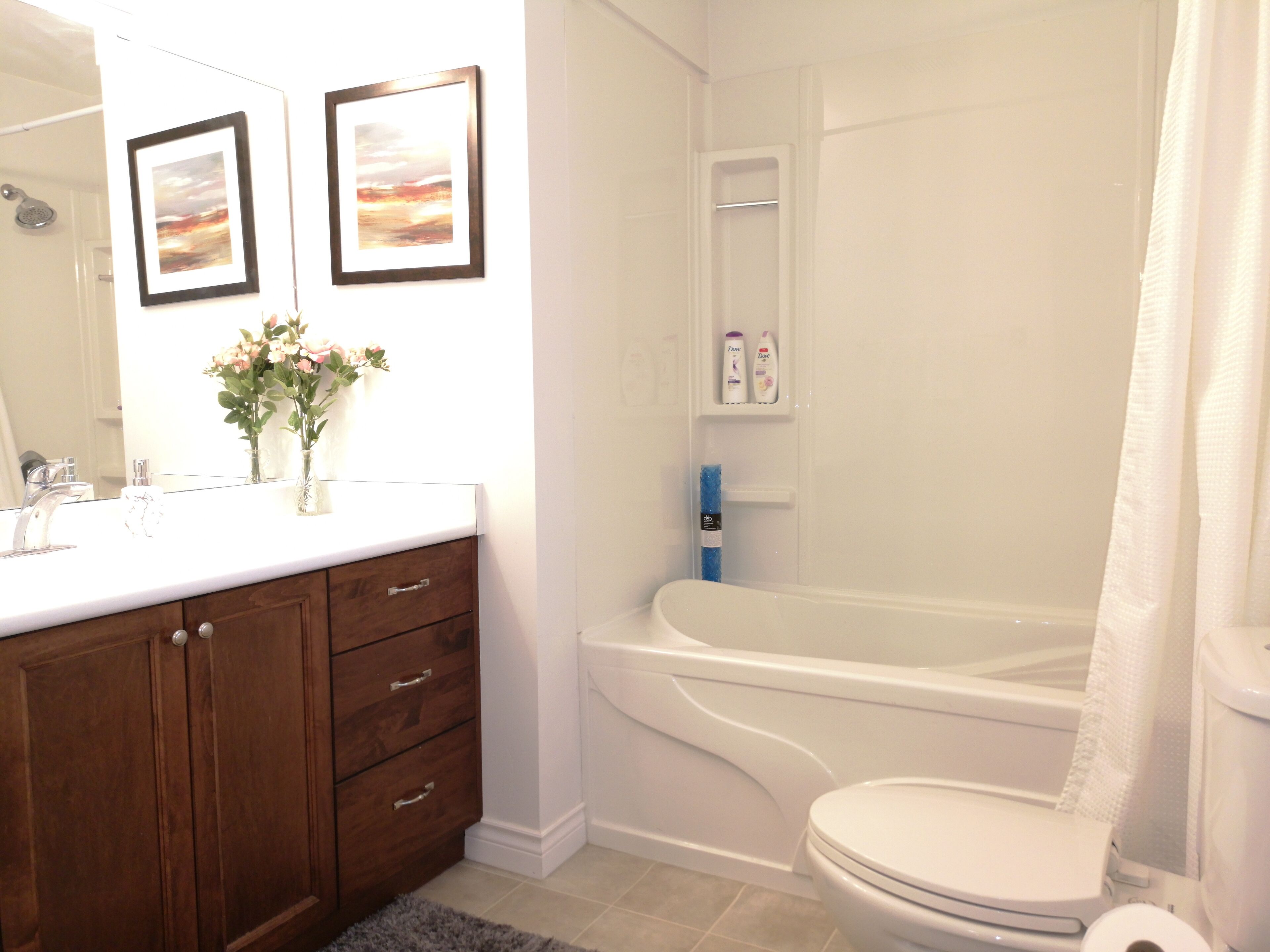 A bathroom with a white sink, wooden vanity, two framed pictures, a shower, and a toilet.