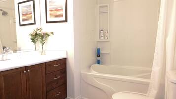 A bathroom with a white sink, wooden vanity, two framed pictures, a shower, and a toilet.