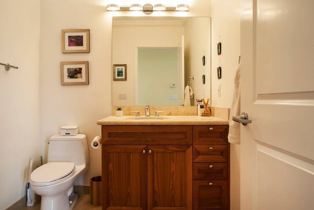 A bathroom with a toilet, sink, vanity, and mirror. There are framed pictures on the wall and a towel rack.