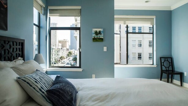 A bedroom with a large bed, a view of buildings through the window, and a chair. - Amazing Large Central Modern Flat - Great for Work + Families (San Francisco)