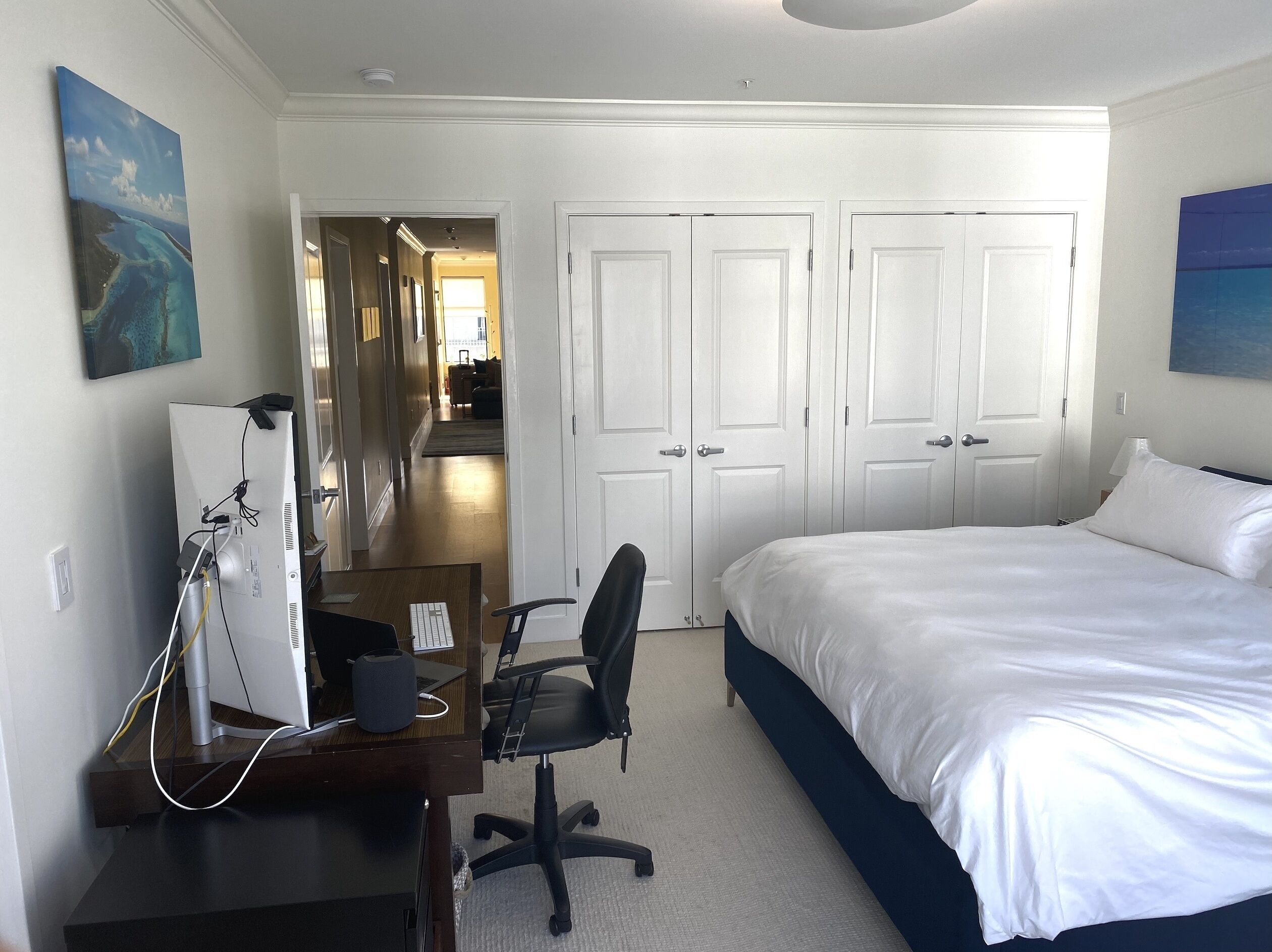 A hotel room with a bed, desk, chair, and two doors.