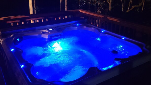 A hot tub with blue lighting, surrounded by trees.