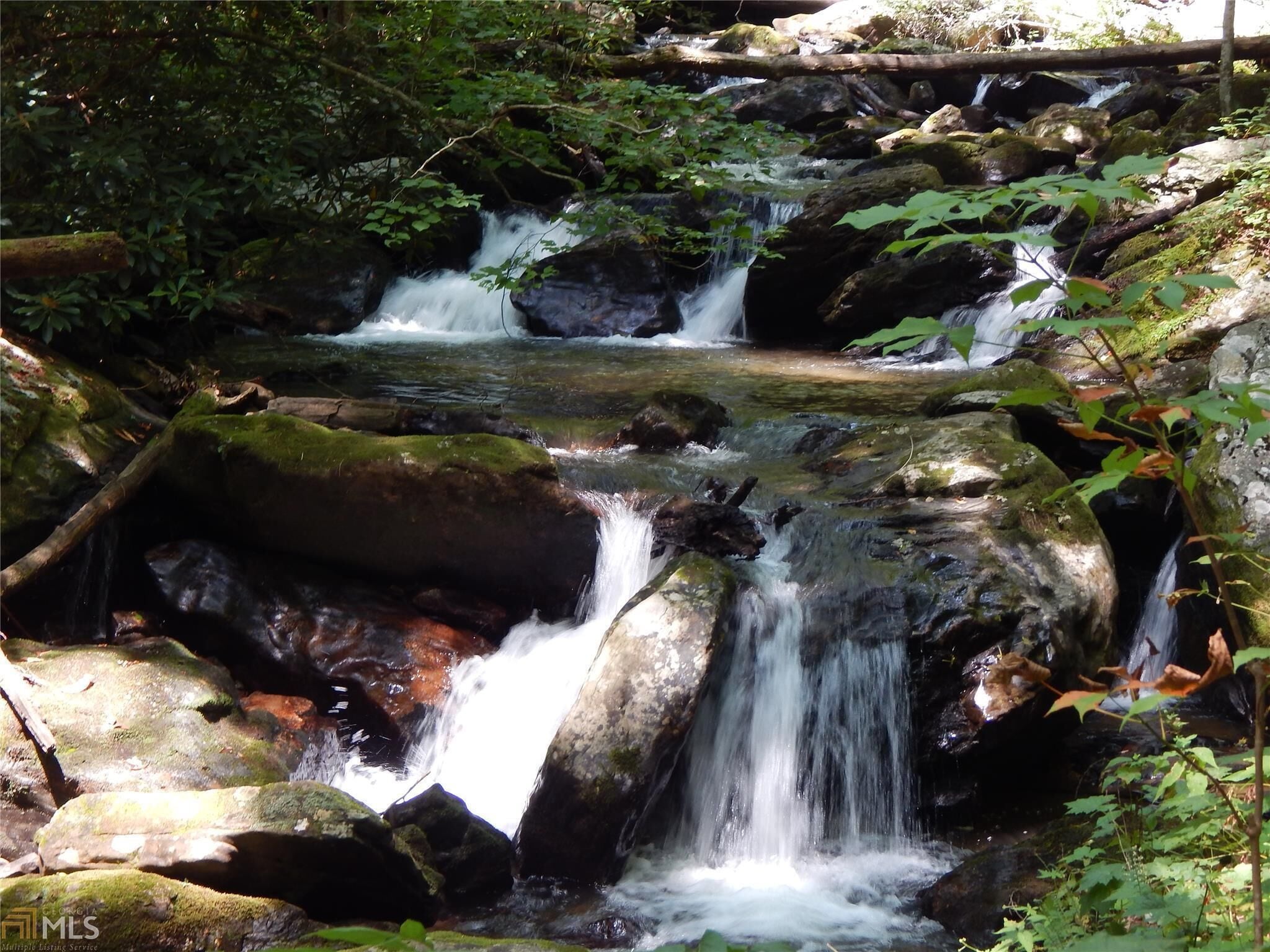 A natural waterfall in a forested area with rocks and greenery.