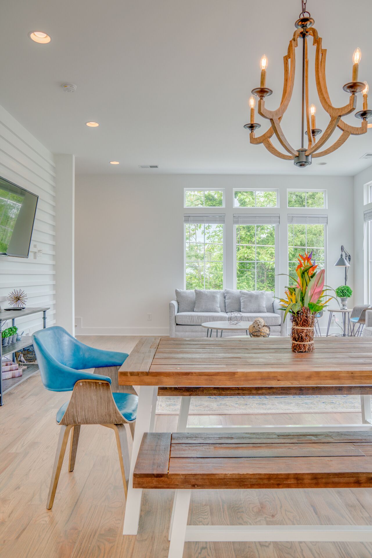 A modern living room with a wooden dining table, blue chairs, a grey sofa, and a chandelier.