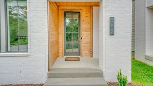 Une entrée moderne avec une porte en bois, un paillasson et une plaque indiquant le numéro de l’unité.