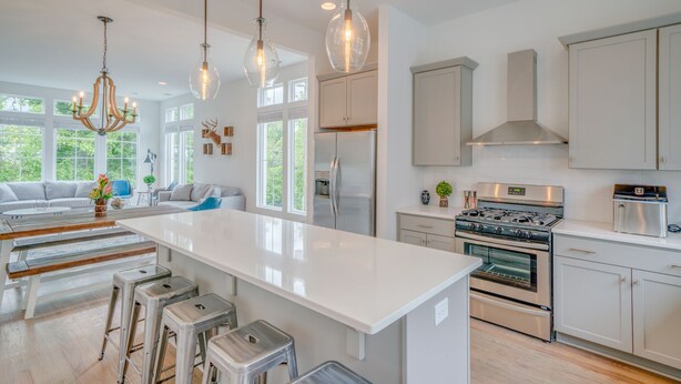 Une cuisine moderne dotée d’un îlot central, d’appareils électroménagers en acier inoxydable et de luminaires suspendus.