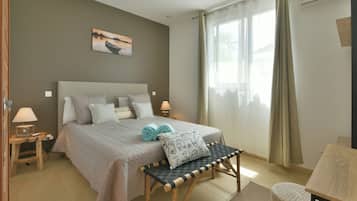 A bedroom with a bed, bedside lamps, a bench, a painting, and a window with curtains.