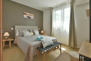 A bedroom with a bed, bedside lamps, a bench, a painting, and a window with curtains.