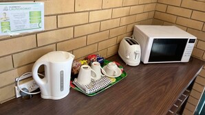 A kitchenette with a microwave, toaster, kettle, and tea set on a wooden counter. - Grand Hotel Motel (Clermont)