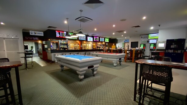 A billiards room with two pool tables, a bar area with neon signs, and a restaurant in the background. - Grand Hotel Motel (Clermont)