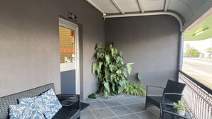 A covered outdoor seating area with a bench and chairs, a potted plant, and a door leading to a building. - Grand Hotel Motel (Clermont)
