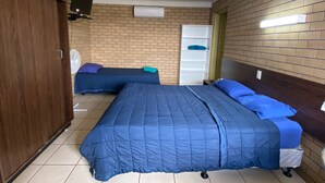 A bedroom with two beds, a wardrobe, a TV, and a shelf unit. - Grand Hotel Motel (Clermont)