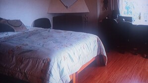 Ett hotellrum med en stor säng, ett skrivbord, en stol och ett fönster med gardiner.