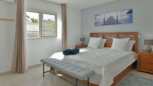 Une chambre à coucher comprenant un lit, un banc, deux tables de chevet, un tableau accroché au mur et une fenêtre avec des rideaux.