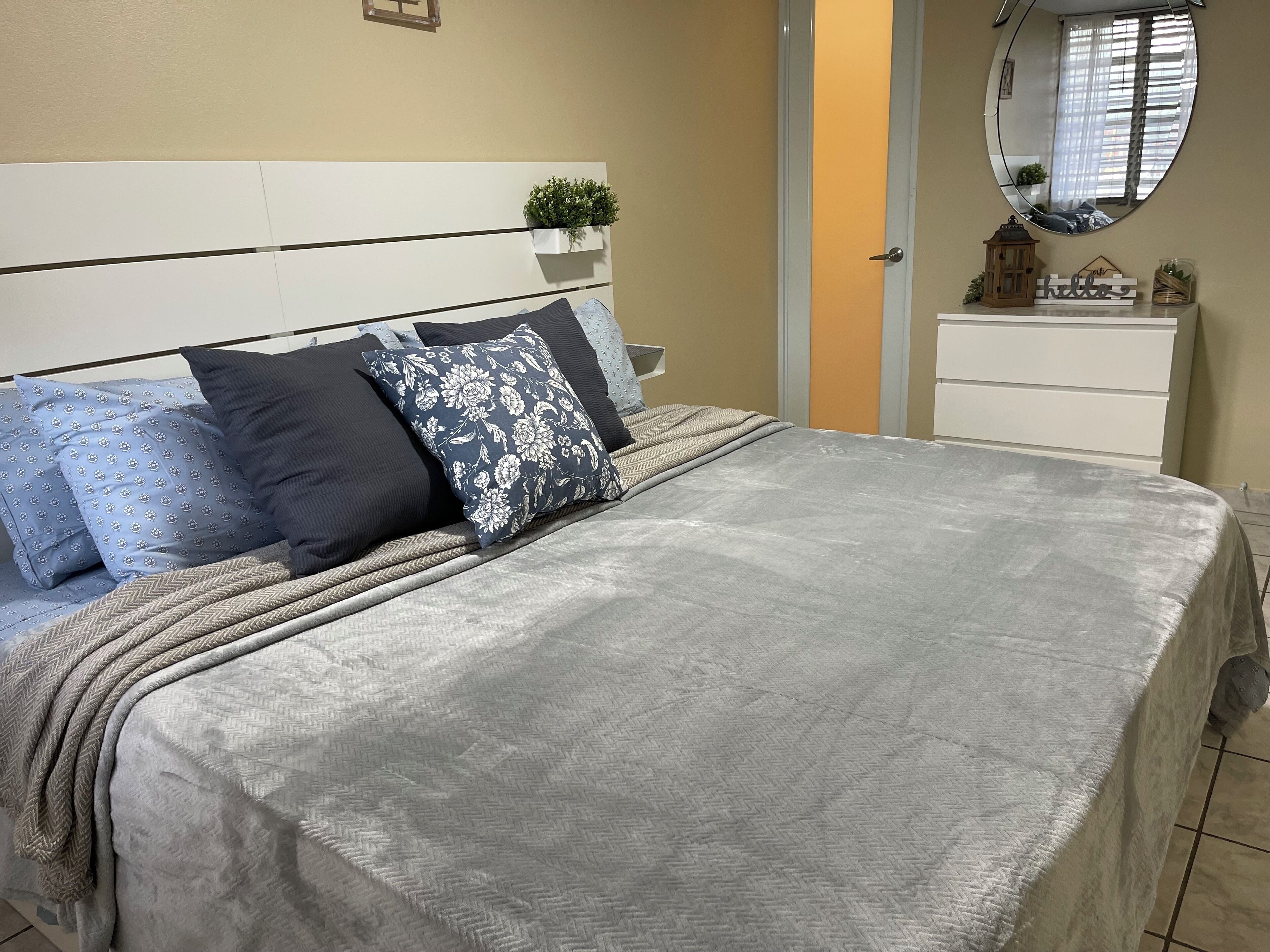 A neatly made bed with a grey quilt, blue patterned pillows, and a grey throw blanket.