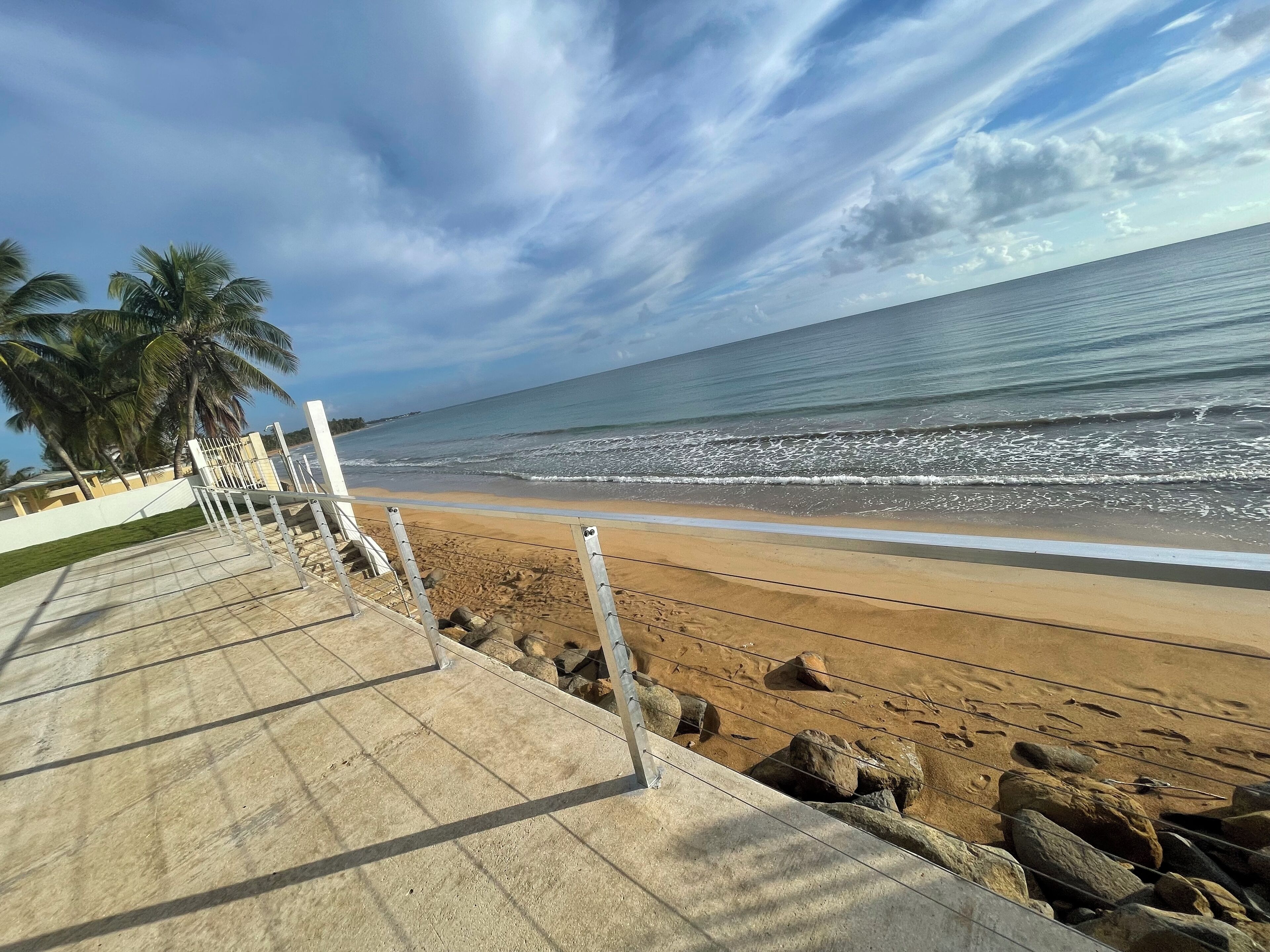 A beach with a concrete walkway, palm trees, and a clear sky.