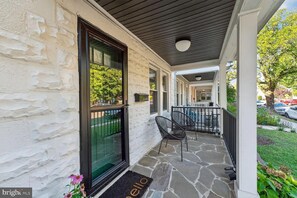 A covered porch with a stone floor, a black-framed door, and two chairs.